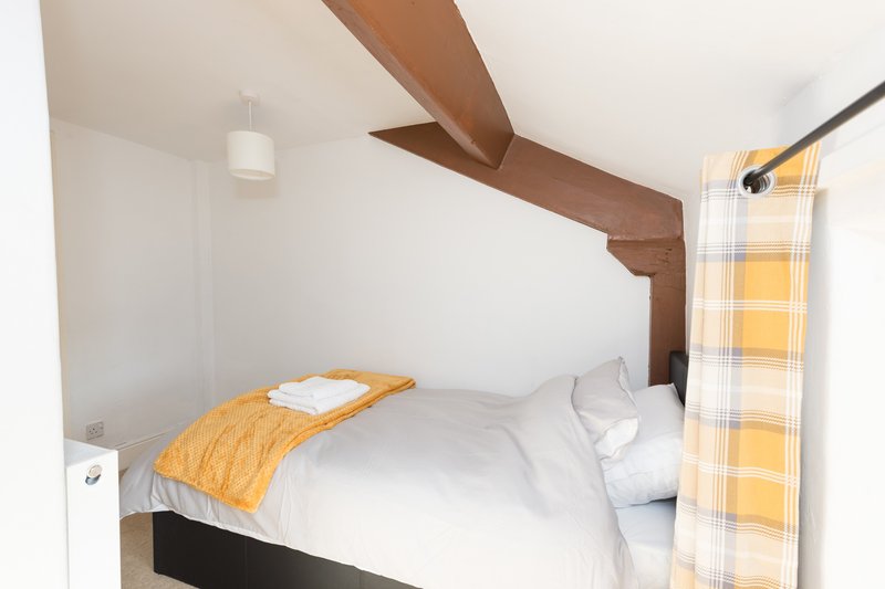 Cozy bedroom with single bed, white bedding, yellow throw, wooden beams and window