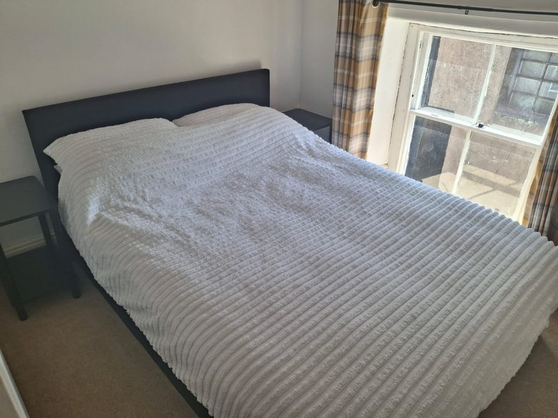Bedroom with dark headboard bed, striped duvet, and window with curtains