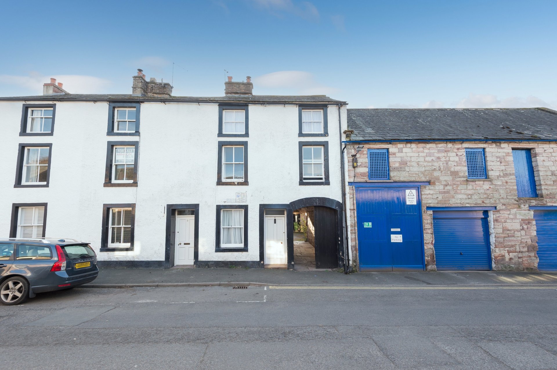 White and stone terraced houses with blue doors and parked car on street