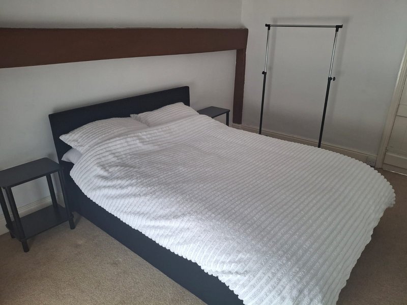 Bedroom with double bed, dark headboard, white bedding, bedside table and wardrobe