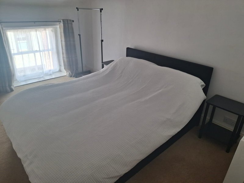 Bright bedroom with double bed, black headboard, window with curtains and bedside table