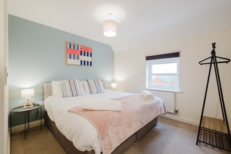 Modern bedroom with double bed, mint green accent wall, bedside tables, and coat stand