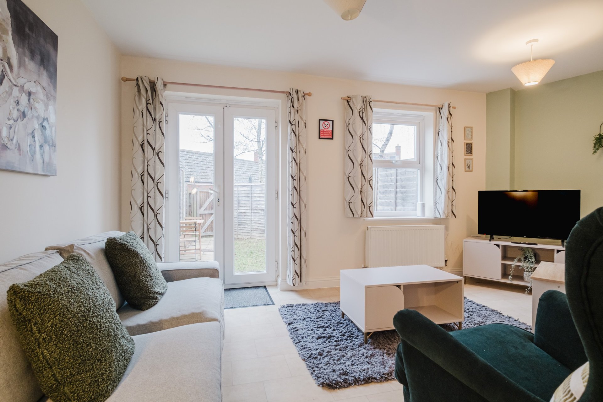 Bright living room with sofa, armchair, TV, patio doors and winter garden view