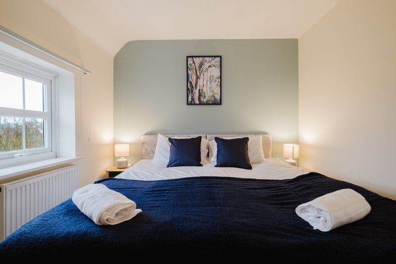 Bedroom with double bed, navy bedding, white pillows, blue cushions and wall-mounted framed artwork