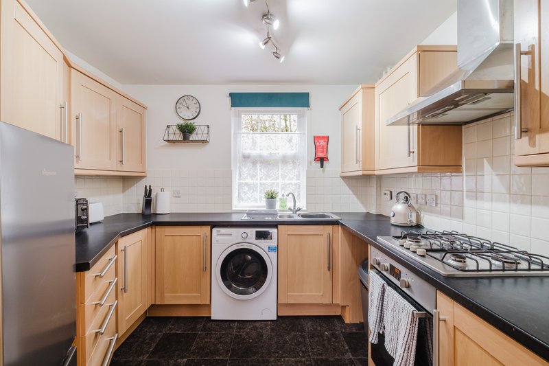 Modern kitchen with wooden cabinets, black countertops, gas range, and integrated washing machine