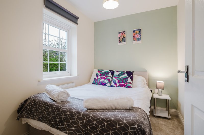 Bright bedroom with double bed, patterned bedding, window with garden view, and mint-green accent wall