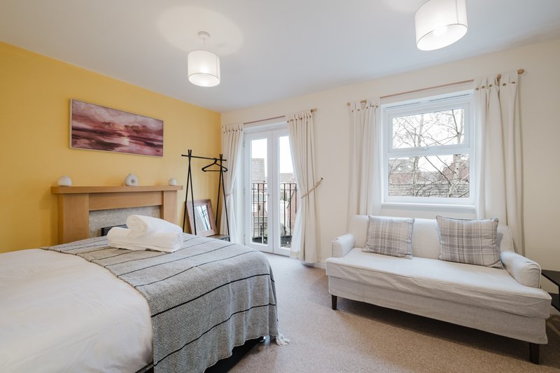 Bright bedroom with yellow walls, two beds, wooden headboard, and large windows with curtains
