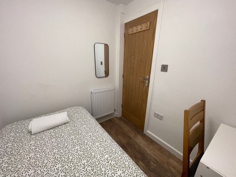 Small bedroom with single bed, wooden door, mirror, radiator and wooden flooring