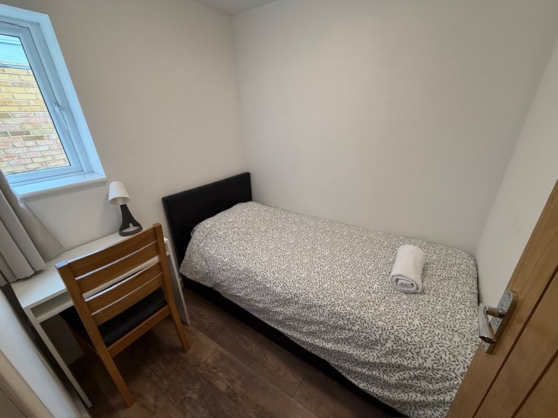 Small bedroom with single bed, wooden chair, skylight window and dark flooring