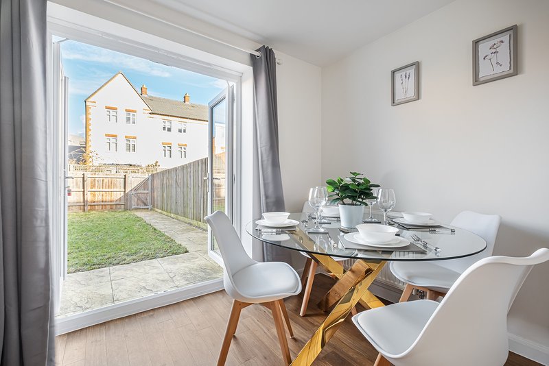 Dining area with round glass table, white chairs, and view through patio doors to garden