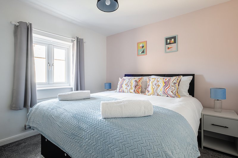 Bright bedroom with double bed, patterned bedding, blue lamps, and window with grey curtains