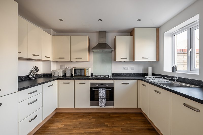 Modern kitchen with cream cabinets, black countertops, built-in oven and wooden flooring