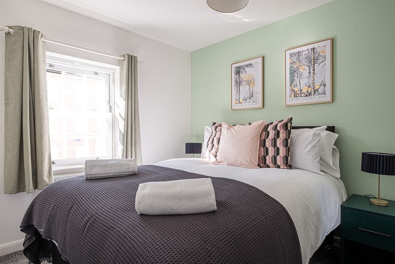 Bedroom with double bed, sage green accent wall, framed prints, and window with curtains