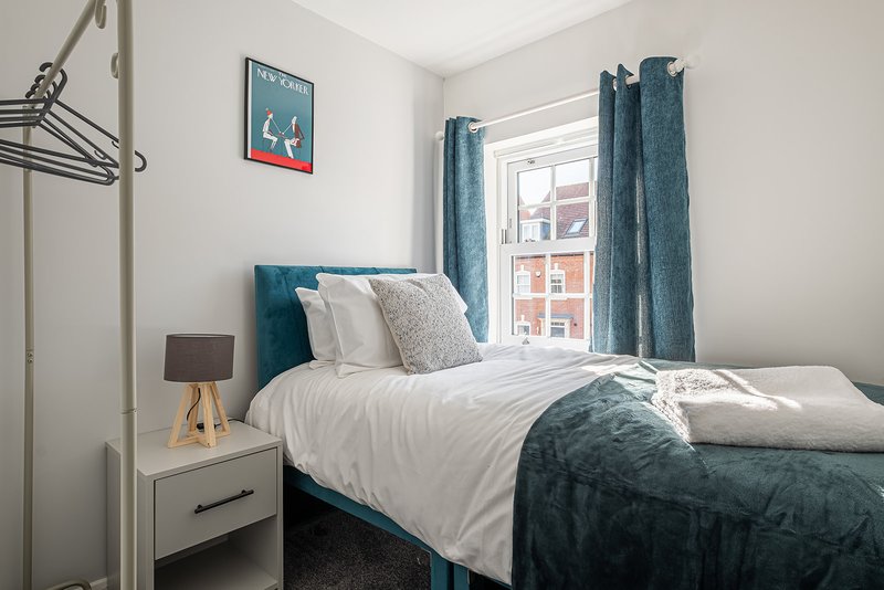 Bright bedroom with teal upholstered bed, white bedding, wooden nightstand and blue curtains