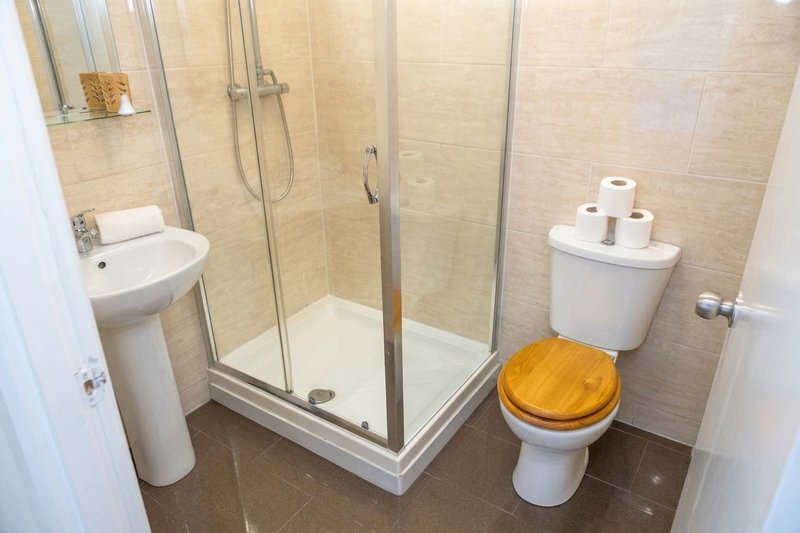 Modern bathroom with shower enclosure, pedestal sink, and toilet with wooden seat