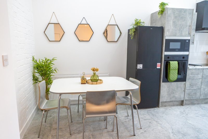 Modern kitchen dining area with white table, metallic chairs, hexagonal wall mirrors, and black appliances