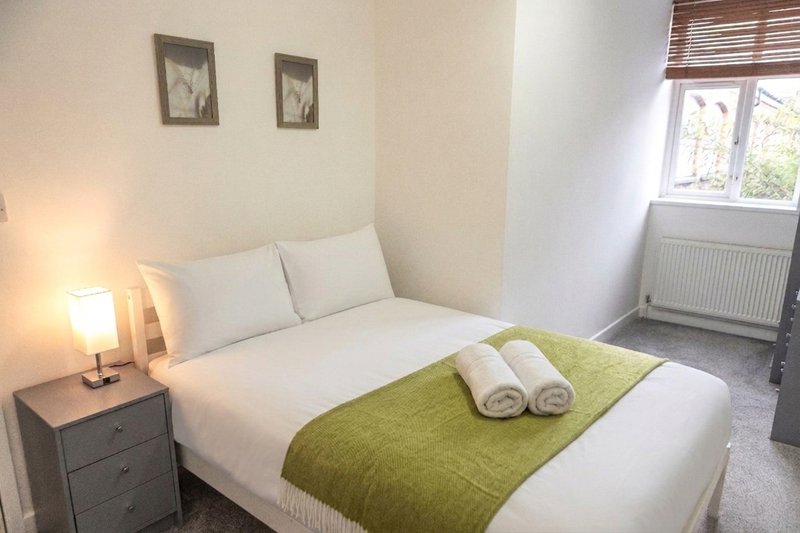 Bright bedroom with double bed, green throw, white pillows and bedside lamp
