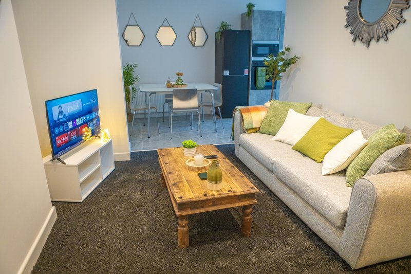 Modern living room with sofa, wooden coffee table, TV, dining area and kitchen visible in background