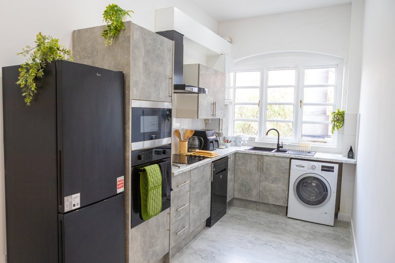 Modern kitchen with black refrigerator, gray cabinetry, washing machine, and window with plants