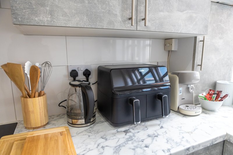 Kitchen countertop with marble surface, wooden utensil holder, appliances and kitchenware