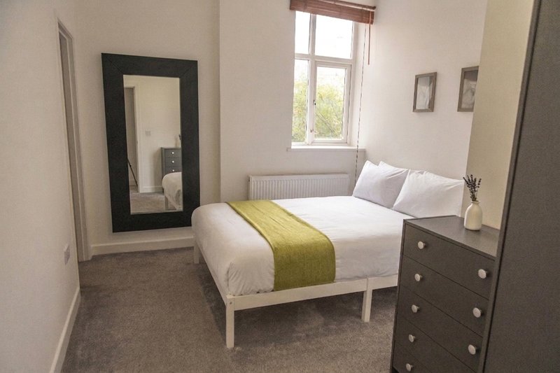 Bright bedroom with double bed, olive green runner, mirror, chest of drawers and window