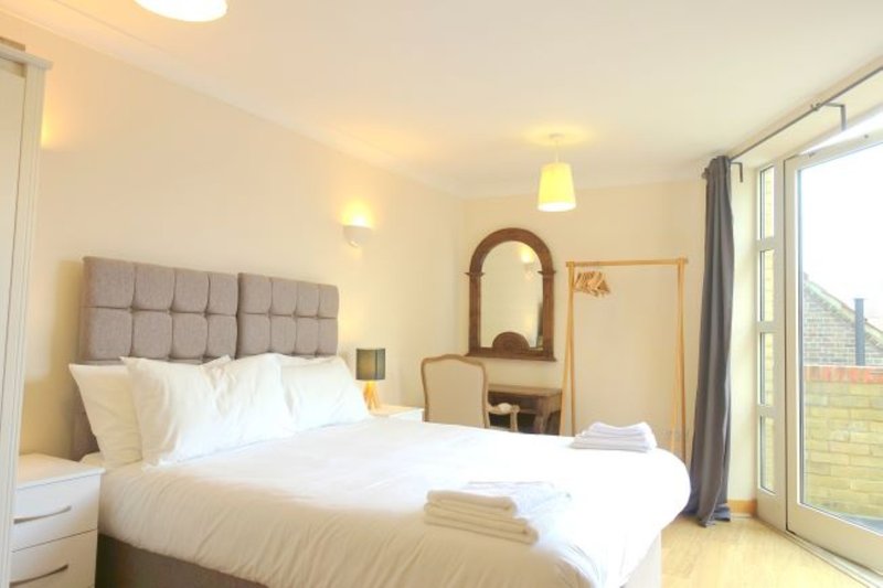 Bright bedroom with double bed, upholstered headboard, dressing table and glass doors to outdoor space