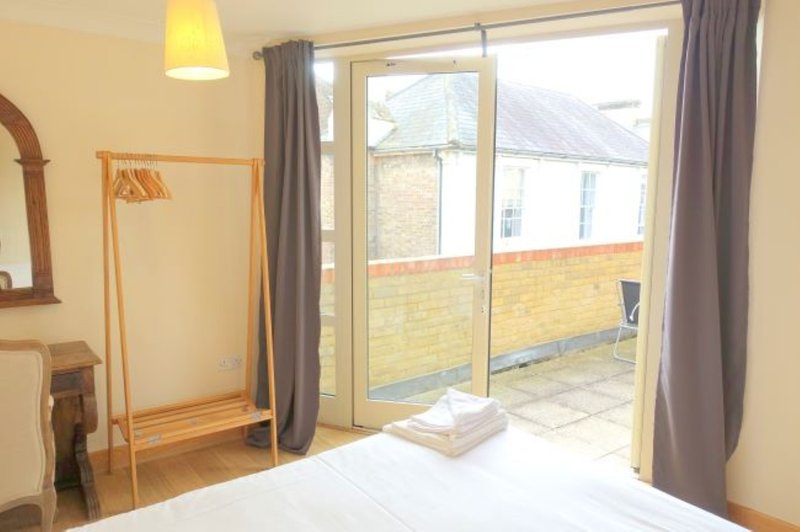 Bright bedroom with double bed, wooden clothing rack, and glass doors opening to patio area
