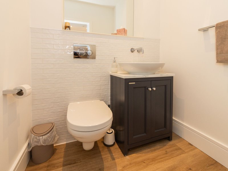 Modern bathroom with toilet, dark vanity, vessel sink, white subway tile, and wooden floor