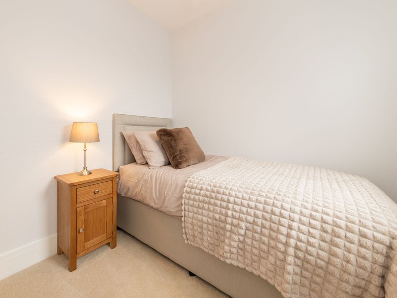 Bedroom with double bed, wooden nightstand, lamp, and neutral bedding
