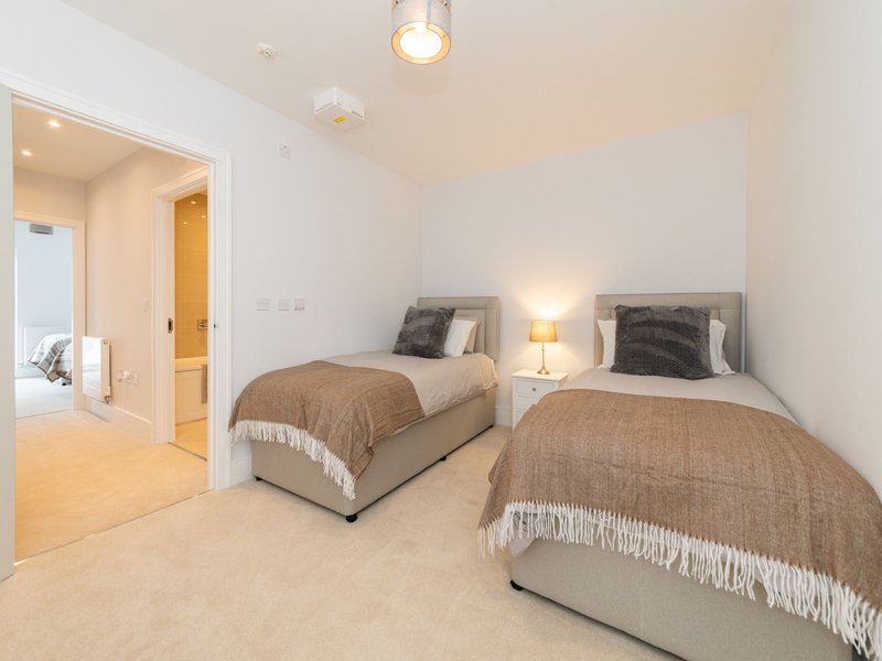 Twin bedroom with two single beds, bedside lamps, cushions and throws, en-suite door visible