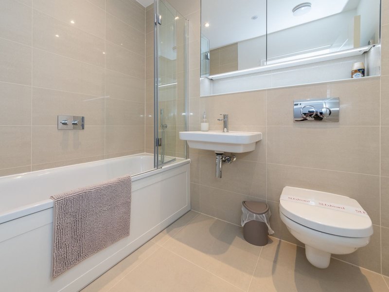 Modern bathroom with bathtub, glass shower screen, wall-mounted sink, and toilet