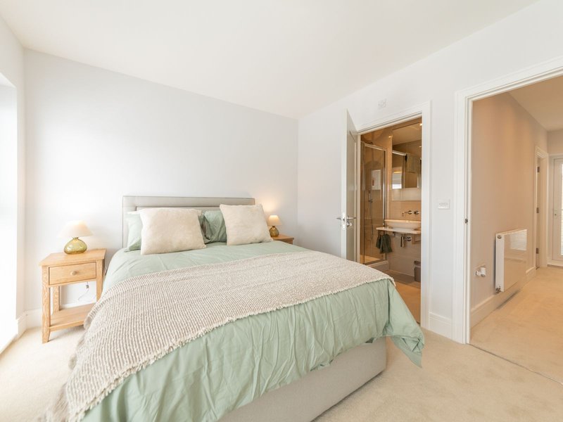 Bright bedroom with double bed, green bedding, wooden nightstand, and ensuite bathroom visible