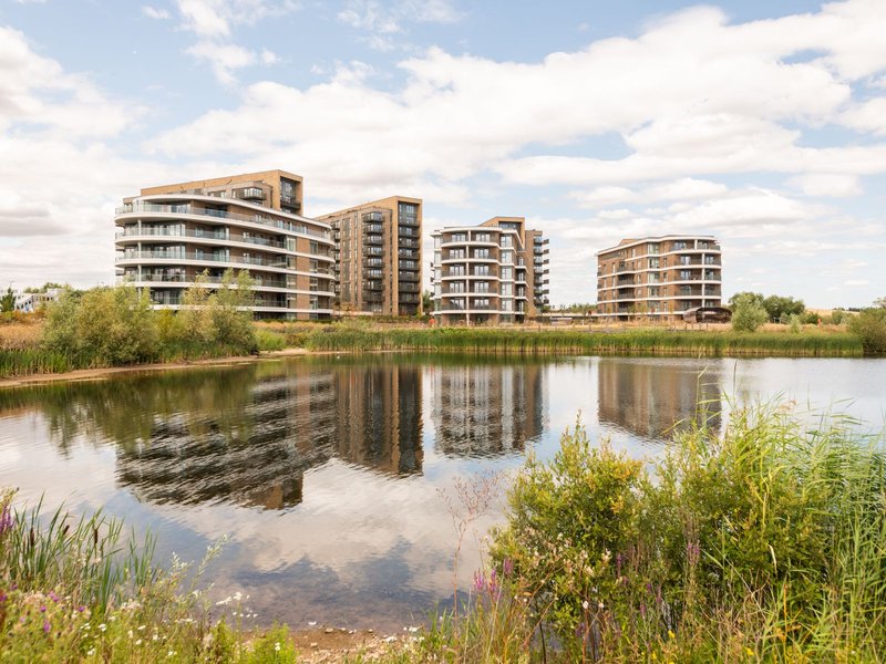 Modern apartment buildings reflected in still water with waterside vegetation and blue sky