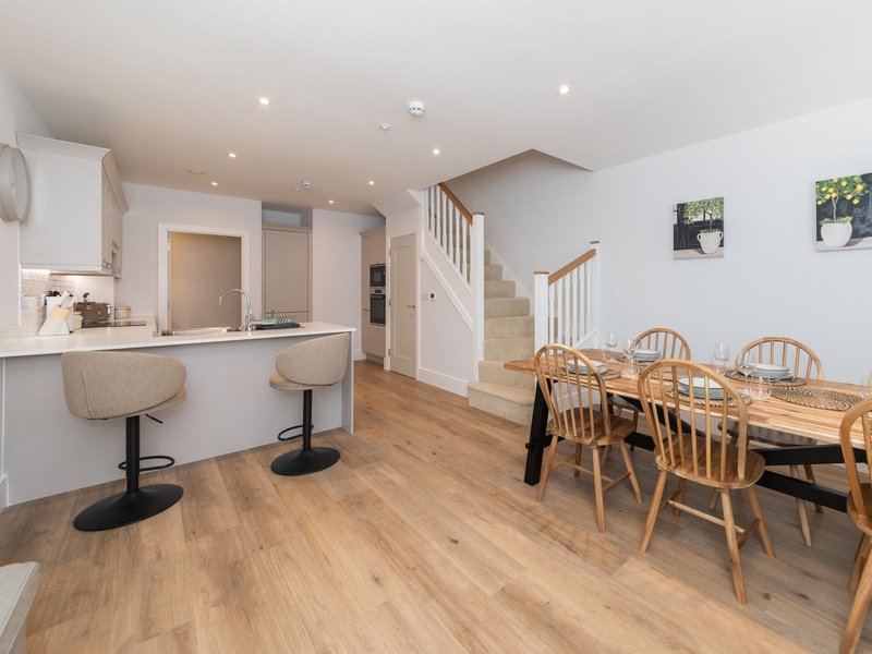 Open-plan kitchen and dining area with wooden flooring, white cabinetry, and wooden dining table with chairs