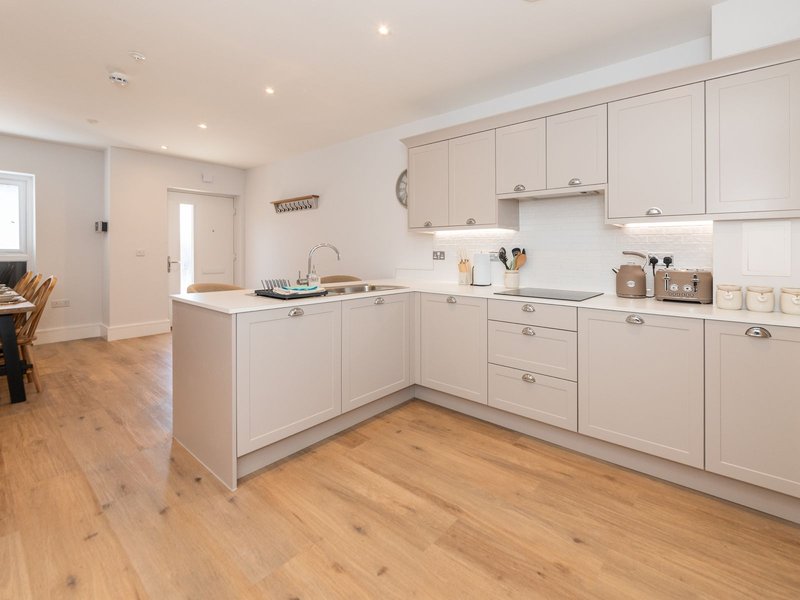 Modern kitchen with cream cabinetry, white countertop, island, wooden flooring and open-plan living area