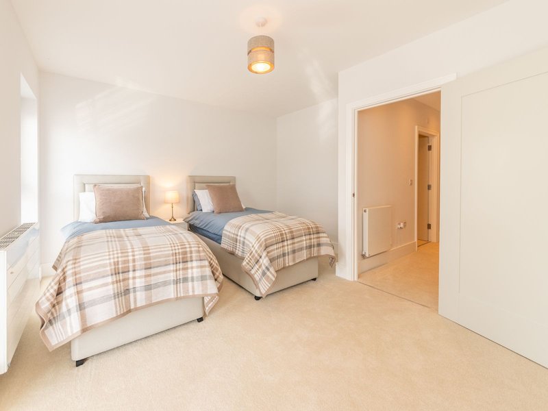 Bright twin bedroom with two single beds, plaid bedding, side lamps and cream carpet
