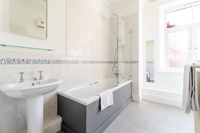 Bathroom with pedestal sink, bath tub, shower screen and window with natural light