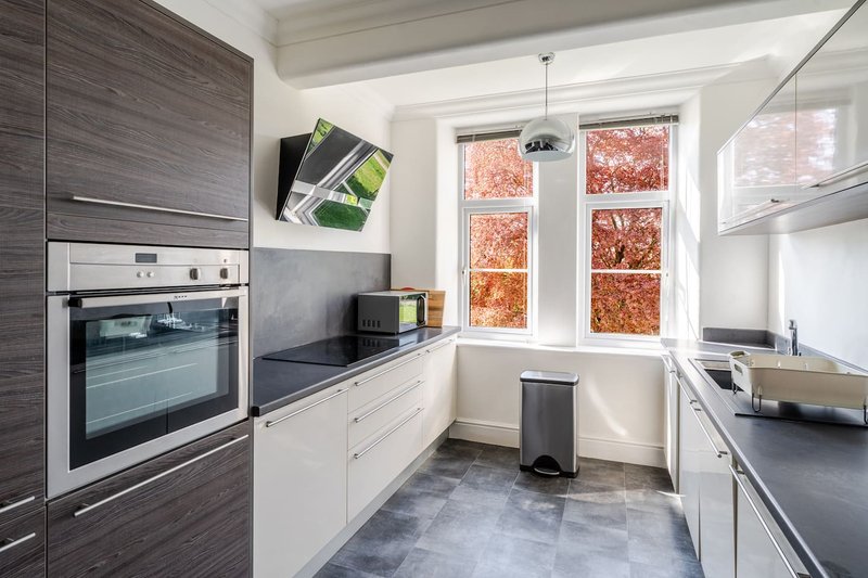 Modern kitchen with integrated appliances, dark countertops, white cabinetry and windows overlooking garden