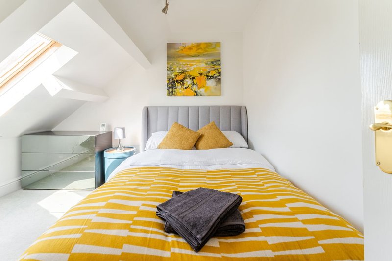 Bright attic bedroom with yellow striped bedding, grey headboard, and skylight window