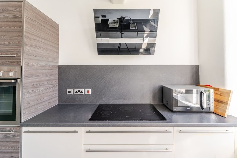 Modern kitchen with dark grey countertop, induction hob, white cabinetry and wooden accents