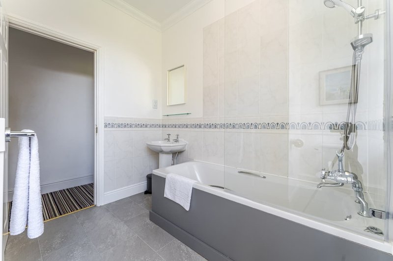 Modern bathroom with grey and white bathtub, pedestal sink, shower enclosure and towel rail