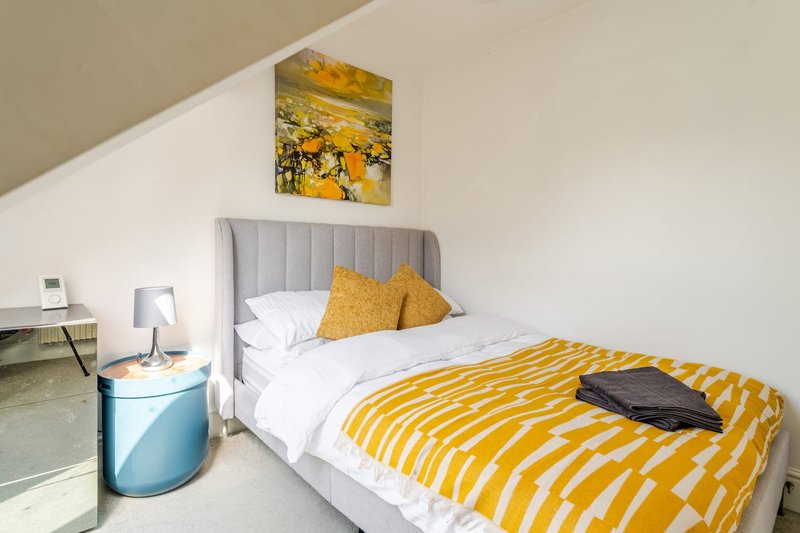 Bright bedroom with single bed, yellow striped bedding, grey headboard, and wall art