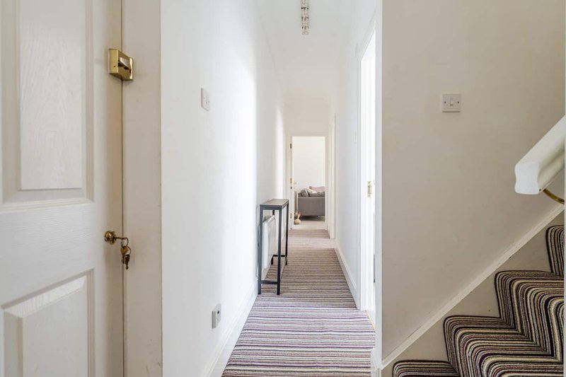 Bright hallway with white doors, striped carpet runner, and staircase with patterned runner