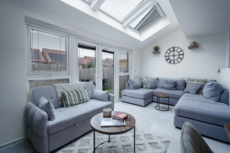 Modern sunroom with grey upholstered seating, round coffee table, skylight and garden views