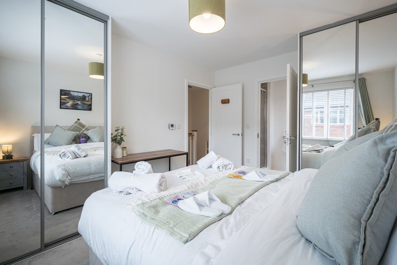 Modern bedroom with double bed, mirrored wardrobes, bedside lamps and window with shutters