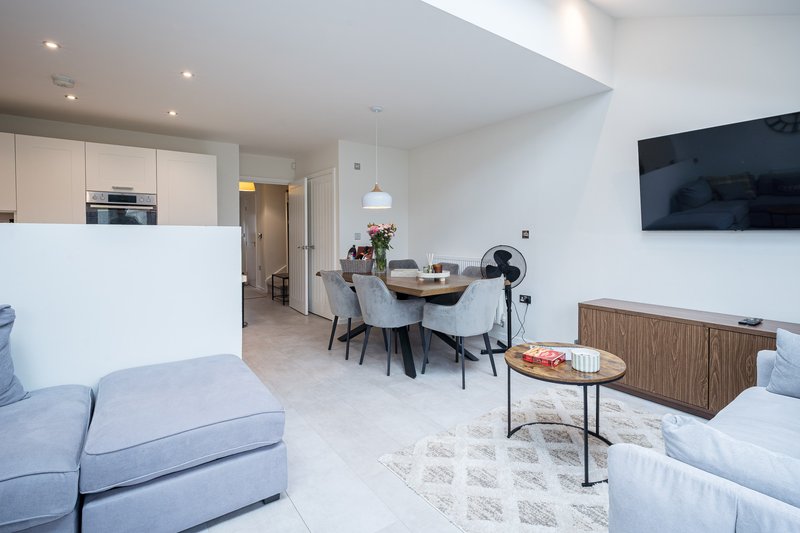 Open-plan living area with light blue sofas, dining table, kitchen, and wall-mounted TV