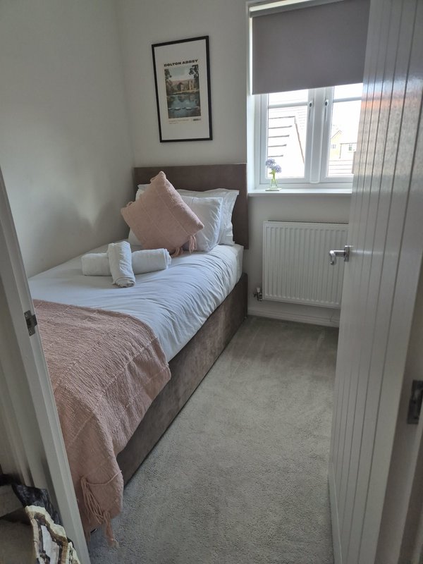 Small bedroom with single bed, pink bedding, framed artwork and window with blind