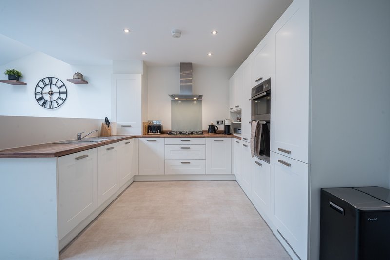 Modern white kitchen with wooden worktops, integrated appliances, and clock wall decoration