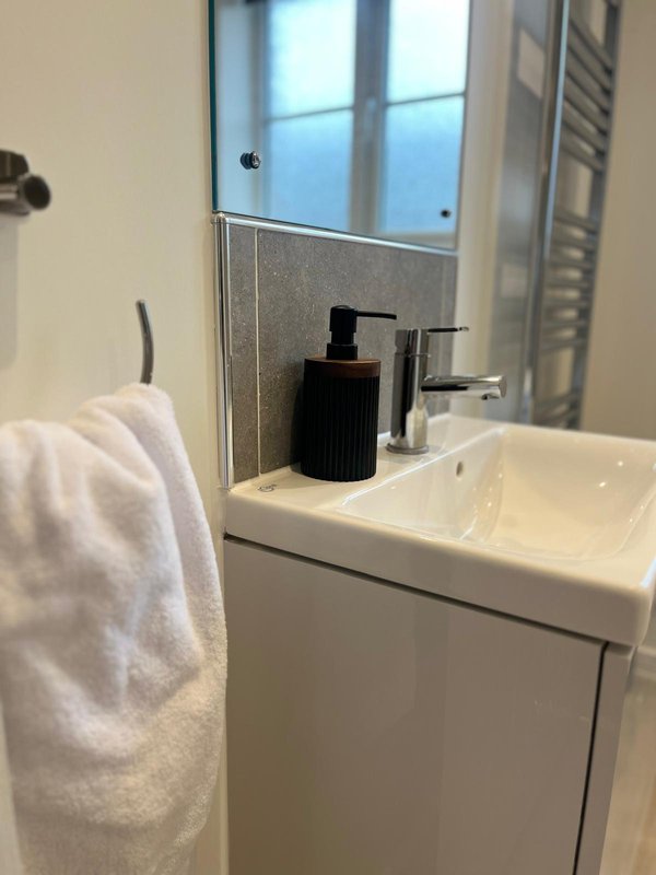 Modern bathroom sink with mirror, black soap dispenser, and white towel hanging on rail