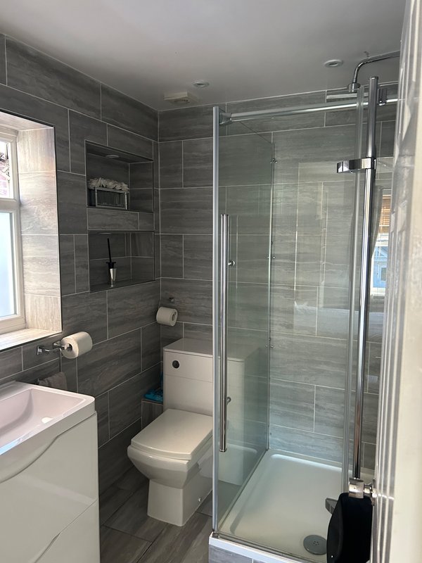 Modern bathroom with grey tile walls, walk-in shower, toilet, and white vanity sink